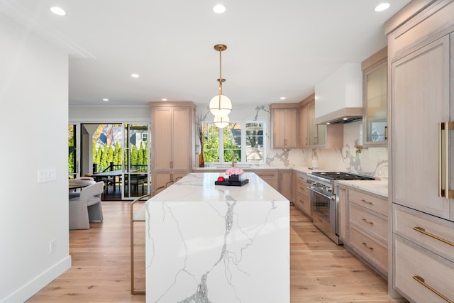 kitchen with light brown cabinets, light wood-style flooring, wall chimney range hood, a center island, and stainless steel range