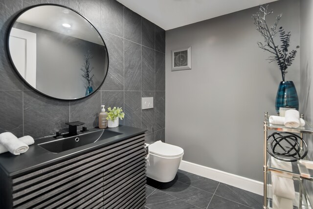 half bath with baseboards, visible vents, toilet, vanity, and tile walls