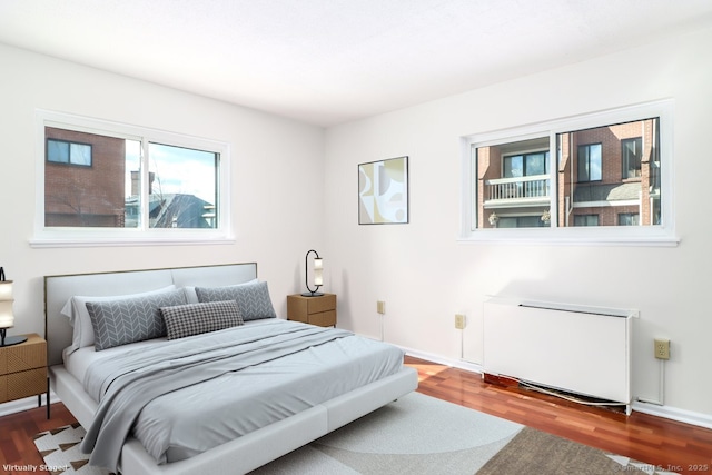 bedroom with radiator heating unit, wood finished floors, and baseboards