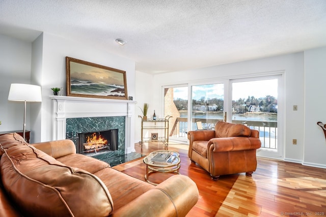 living room with a fireplace, a textured ceiling, baseboards, and wood finished floors