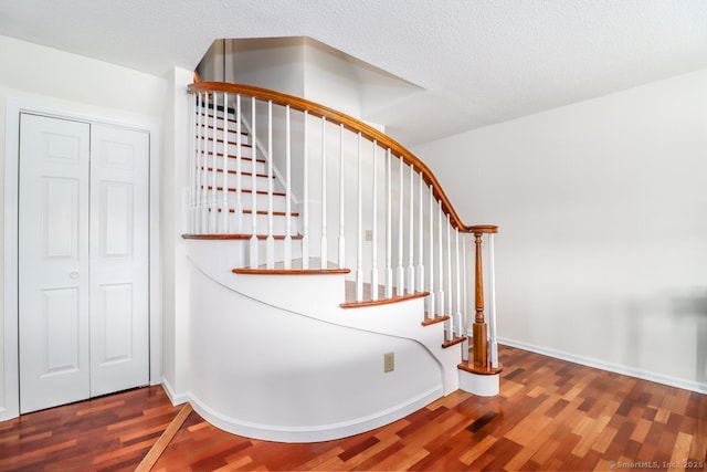 stairway featuring a textured ceiling, baseboards, and wood finished floors