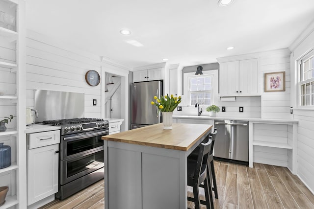 kitchen with a kitchen island, appliances with stainless steel finishes, white cabinets, wooden counters, and wood tiled floor