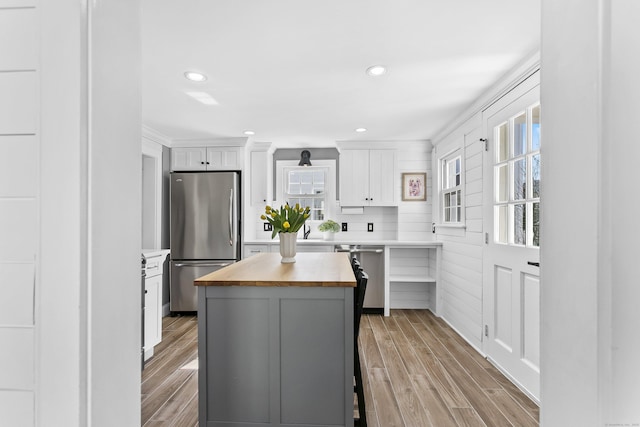 kitchen with a kitchen island, light wood-type flooring, appliances with stainless steel finishes, white cabinetry, and wood counters