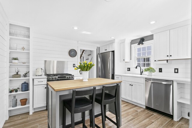 kitchen featuring wood finish floors, a sink, wood counters, white cabinetry, and stainless steel appliances