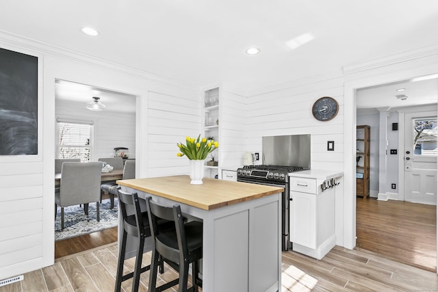 kitchen featuring light wood finished floors, stainless steel range with gas cooktop, crown molding, butcher block counters, and a breakfast bar