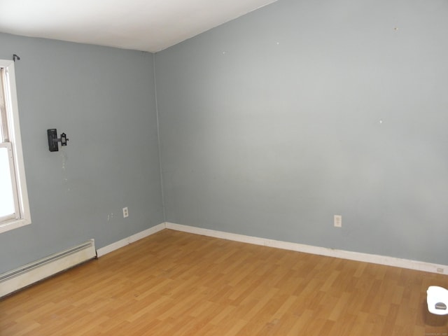 empty room with light wood-type flooring, a baseboard heating unit, and baseboards