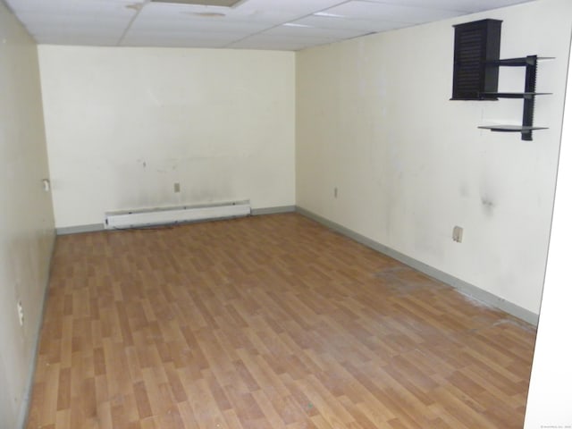 unfurnished room with light wood finished floors, baseboard heating, baseboards, and a drop ceiling