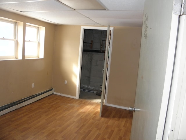 unfurnished room featuring a drop ceiling, baseboards, baseboard heating, and light wood finished floors