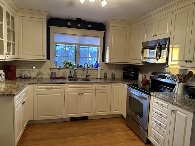 kitchen featuring light wood finished floors, backsplash, appliances with stainless steel finishes, white cabinets, and a sink