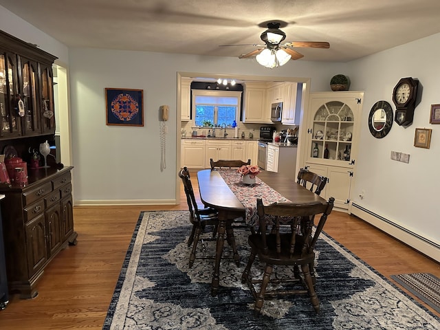 dining area with ceiling fan with notable chandelier, a baseboard radiator, baseboards, and wood finished floors