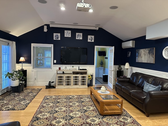 living room featuring vaulted ceiling, an AC wall unit, wainscoting, and wood finished floors