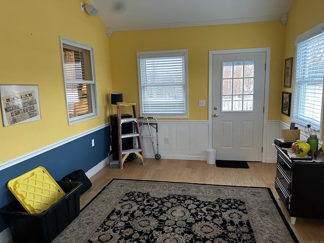 doorway featuring ornamental molding, a wainscoted wall, and wood finished floors