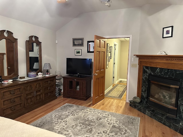 living room featuring lofted ceiling, visible vents, wood finished floors, and a high end fireplace