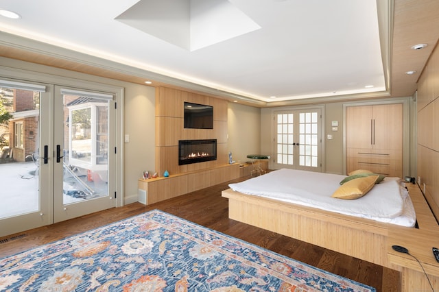 bedroom featuring access to exterior, a tray ceiling, french doors, a large fireplace, and wood finished floors