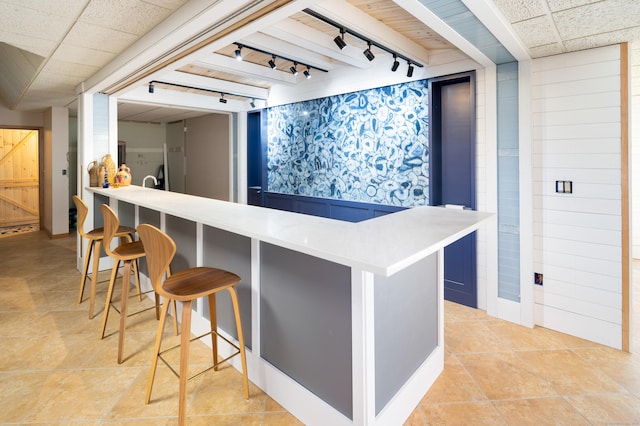 bar with light tile patterned floors, a drop ceiling, and rail lighting