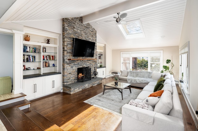 living room with dark wood-style floors, built in shelves, lofted ceiling with beams, a ceiling fan, and a stone fireplace