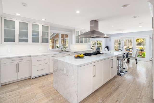 kitchen featuring island range hood, a kitchen island, a sink, white cabinets, and gas stovetop