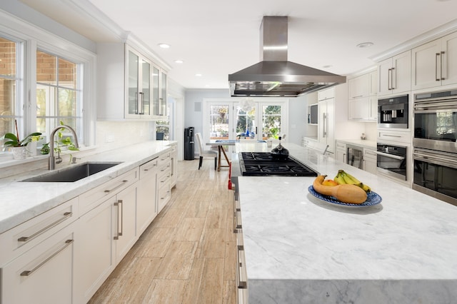 kitchen featuring island range hood, white cabinets, glass insert cabinets, stainless steel appliances, and a sink