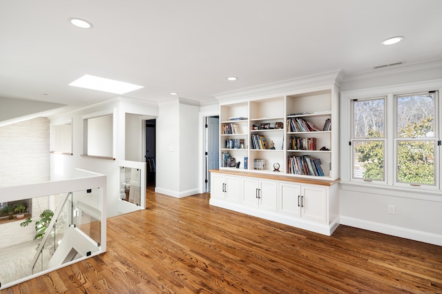 unfurnished room with a skylight, visible vents, wood finished floors, and ornamental molding