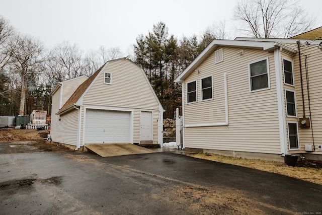 view of side of property with a garage, driveway, an outdoor structure, and a gambrel roof