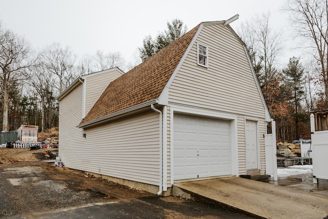 view of side of home with a shingled roof, driveway, and a garage