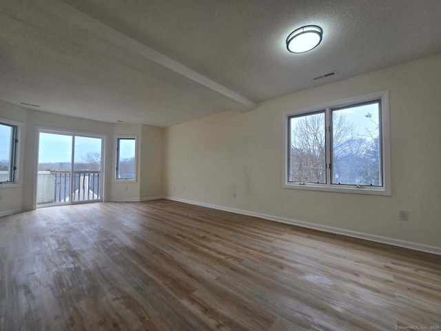 empty room featuring visible vents, a textured ceiling, wood finished floors, beamed ceiling, and baseboards