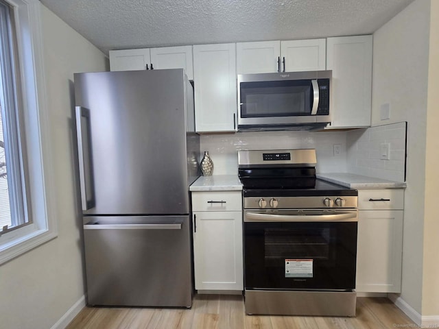 kitchen with stainless steel appliances, light countertops, backsplash, light wood-style floors, and white cabinetry