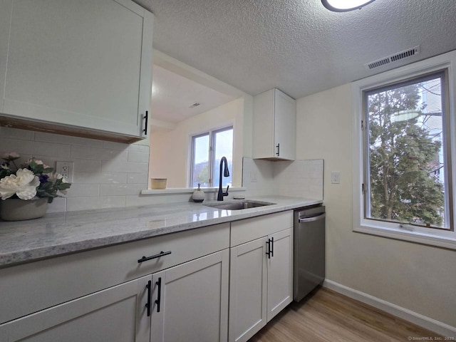 kitchen with visible vents, white cabinets, dishwasher, light wood-type flooring, and a sink