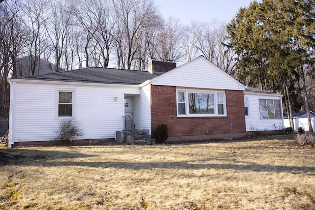 view of front of home featuring brick siding, a chimney, and a front lawn