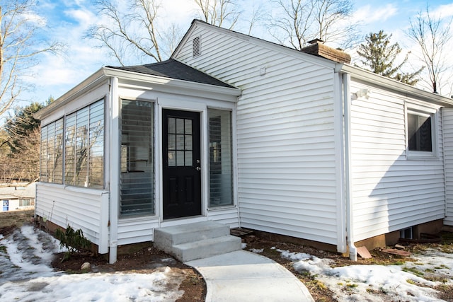 snow covered property entrance with a chimney