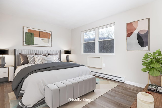 bedroom featuring a baseboard heating unit, baseboards, and wood finished floors