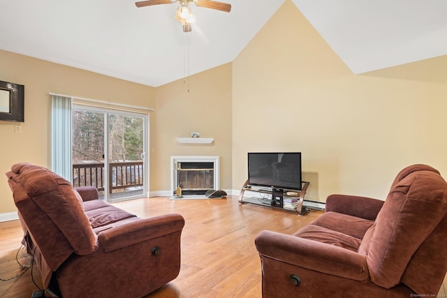 living room with high vaulted ceiling, a fireplace with flush hearth, a ceiling fan, baseboards, and light wood-style floors