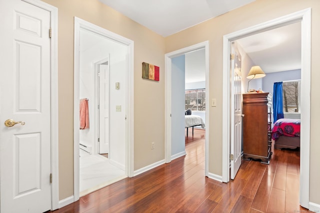 hallway with a baseboard heating unit, wood finished floors, and baseboards