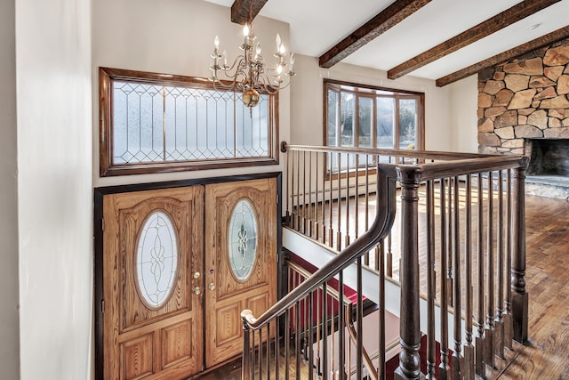 entryway with an inviting chandelier, a baseboard heating unit, a stone fireplace, wood finished floors, and beamed ceiling