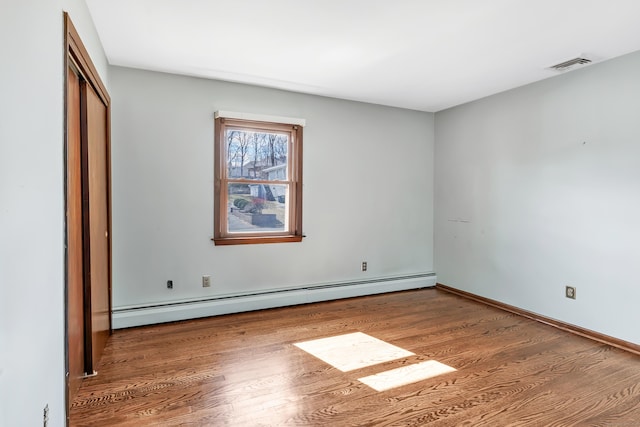 unfurnished bedroom featuring a closet, a baseboard radiator, wood finished floors, and visible vents