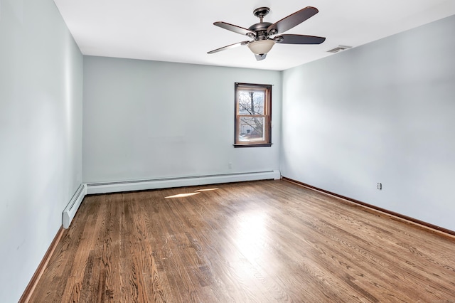 spare room with visible vents, baseboard heating, ceiling fan, wood finished floors, and baseboards