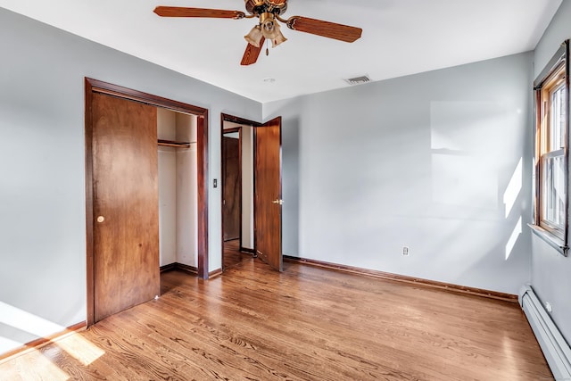 unfurnished bedroom with a closet, visible vents, baseboard heating, wood finished floors, and baseboards