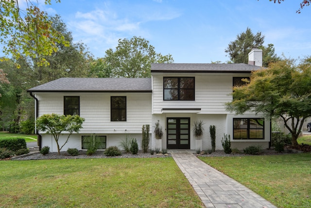 view of front of property with a shingled roof, brick siding, a chimney, and a front lawn