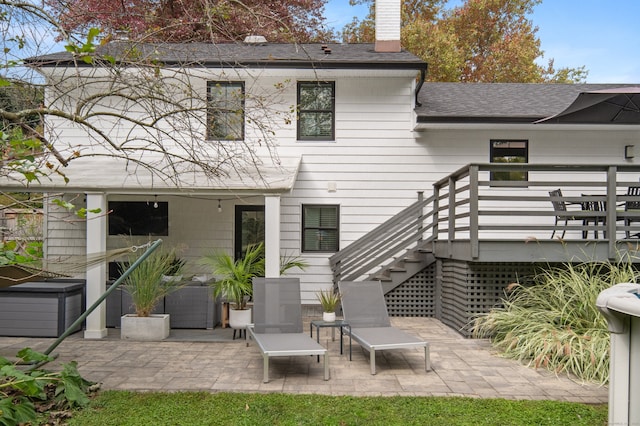 back of property featuring a shingled roof, a patio area, a chimney, and stairs