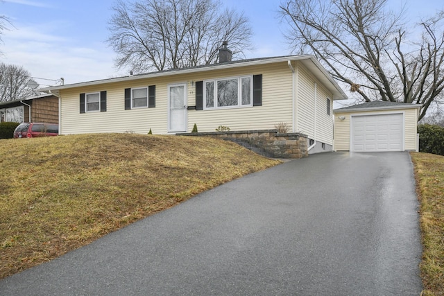 ranch-style home with a garage, a chimney, aphalt driveway, an outbuilding, and a front yard