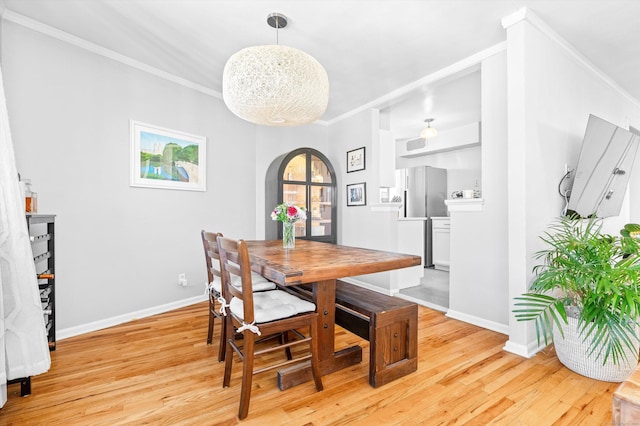 dining room featuring arched walkways, a notable chandelier, ornamental molding, light wood-type flooring, and baseboards