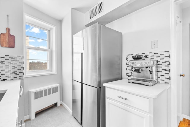 kitchen with visible vents, white cabinetry, backsplash, freestanding refrigerator, and radiator heating unit