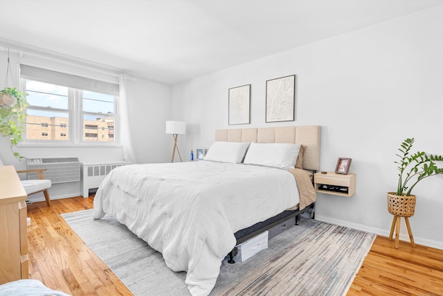 bedroom featuring light wood finished floors, radiator heating unit, and baseboards