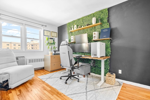 office area featuring an accent wall, baseboards, radiator heating unit, and wood finished floors