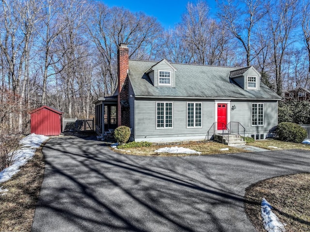 cape cod-style house with an outbuilding, driveway, and a chimney