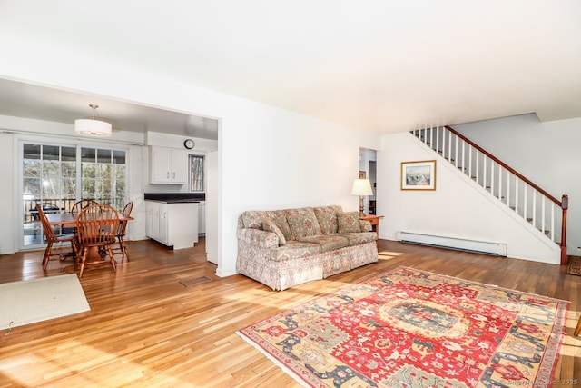 living room with light wood-style flooring, stairs, a baseboard heating unit, and visible vents