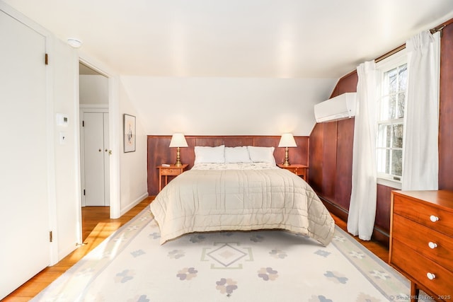 bedroom featuring vaulted ceiling, a wall mounted AC, and light wood-type flooring