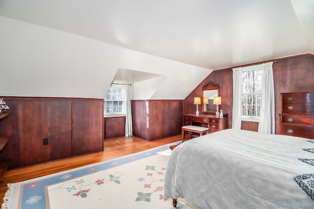 bedroom with lofted ceiling, a wainscoted wall, wood walls, and wood finished floors