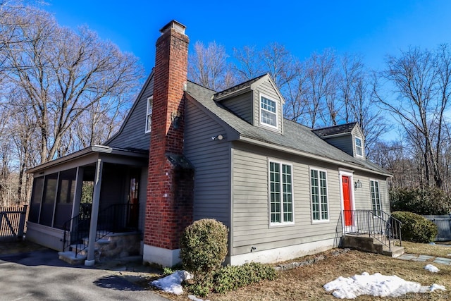 view of side of property featuring a shingled roof, a sunroom, fence, and a chimney