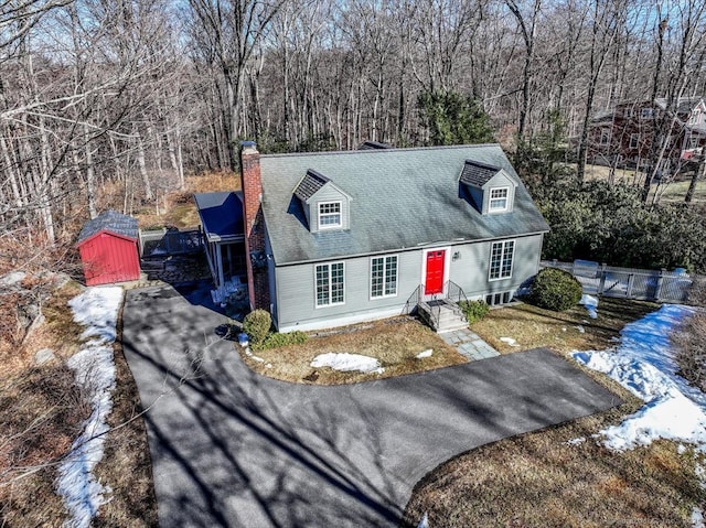 cape cod home featuring entry steps, an outdoor structure, driveway, a storage unit, and a chimney